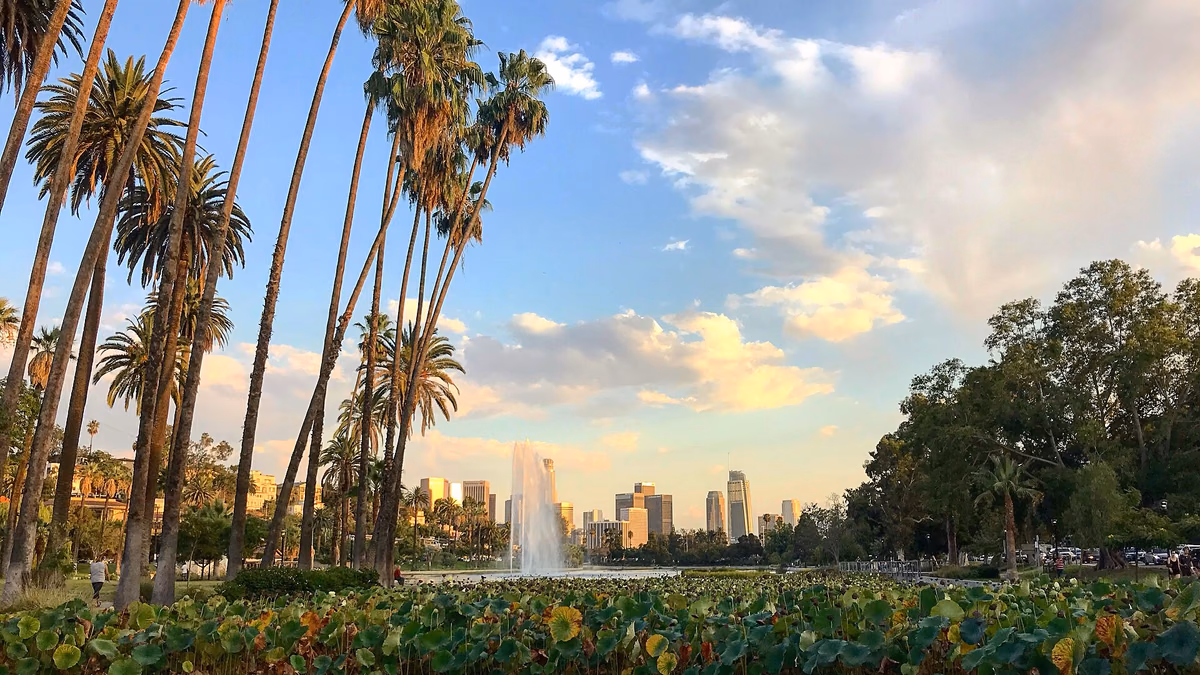 Echo park lake and fountain on a partly cloudy day in Echo Park, Los Angeles, CA with lotus flowers in the foreground and the Downtown Los Angeles skyline in the background,