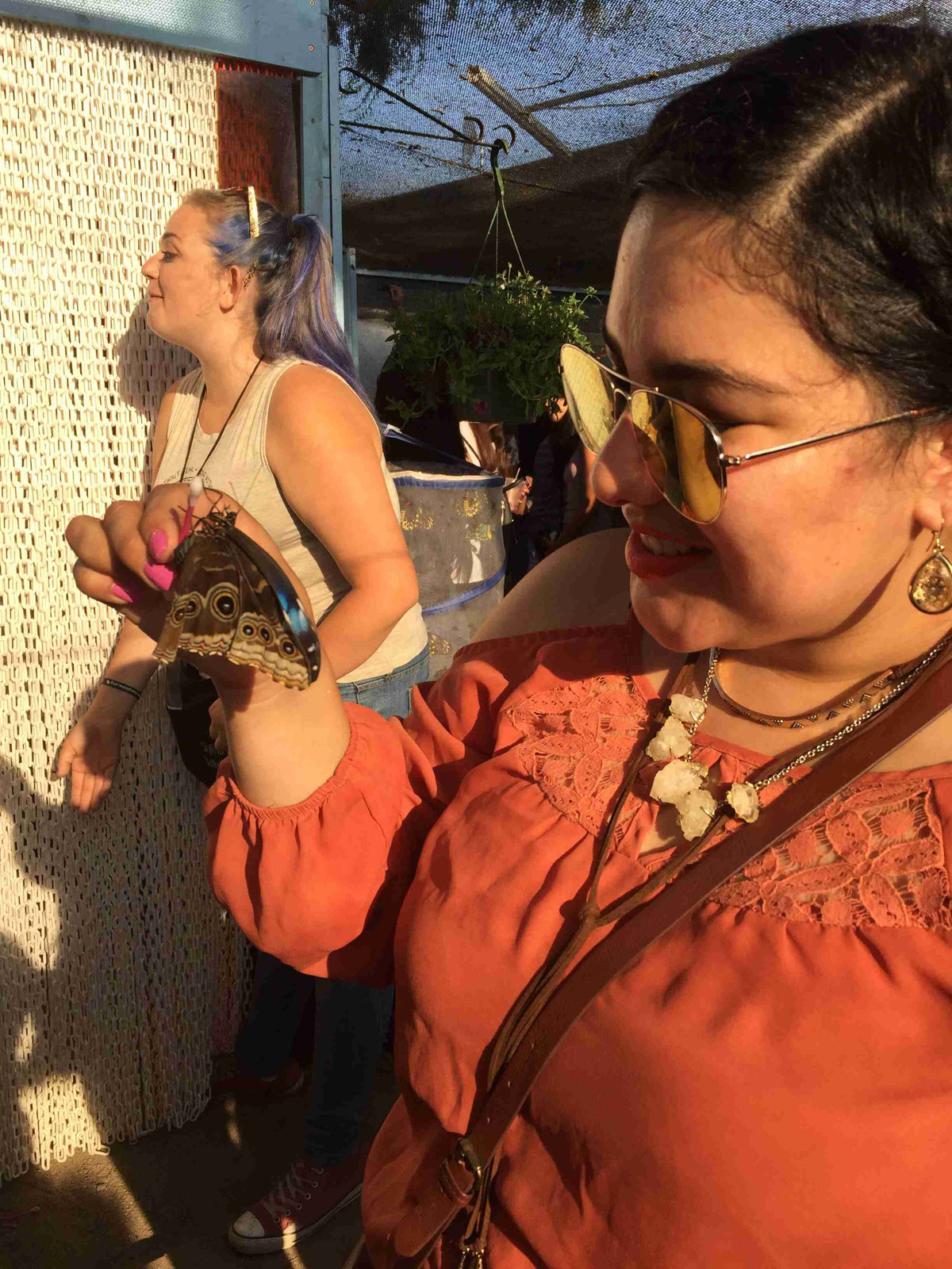 A young Latina women with an orange shirt holding a brown butterfly.