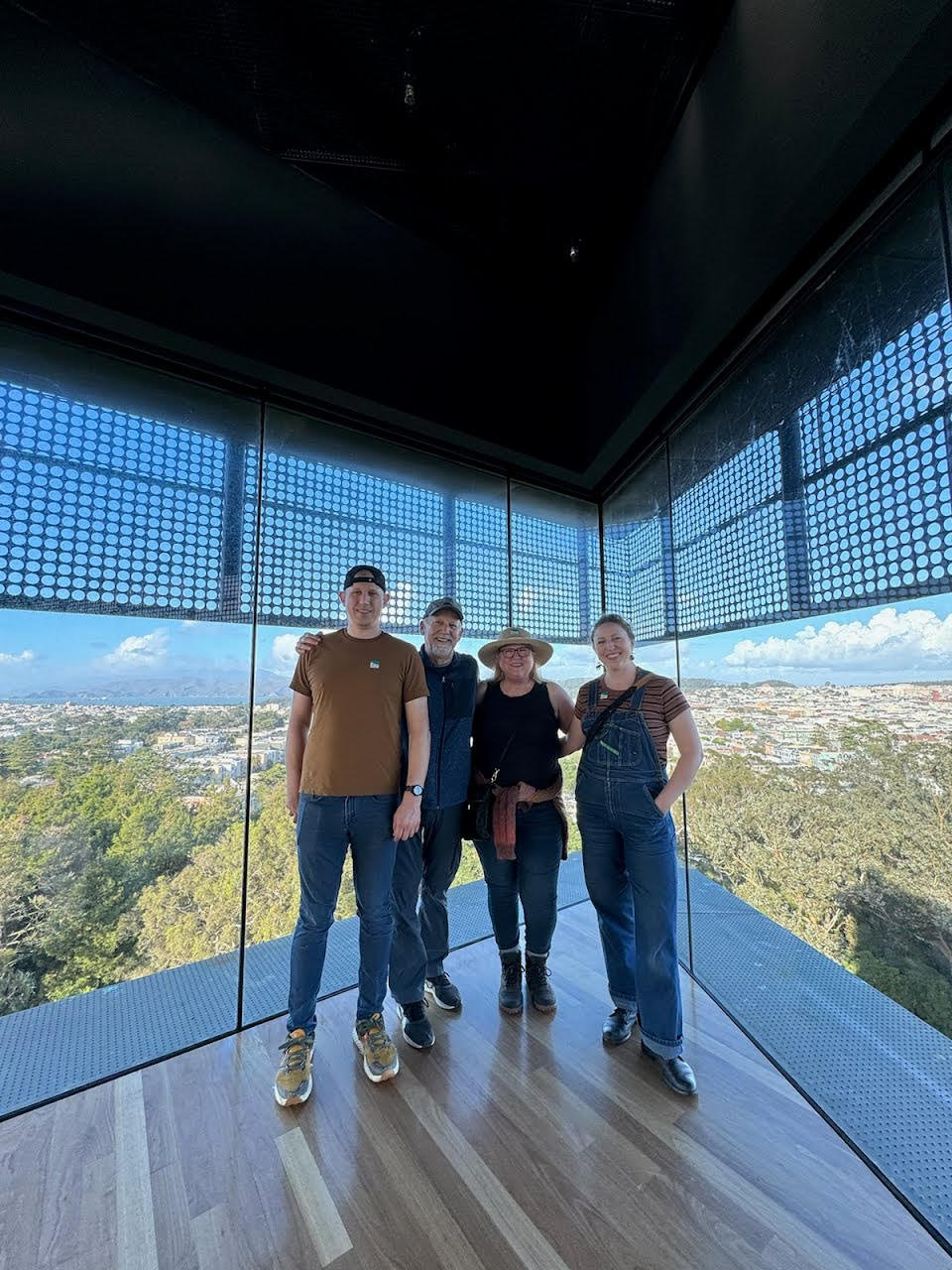 Kevin and his wife with their adult son and daughter in a glass-walled overlook above a city.