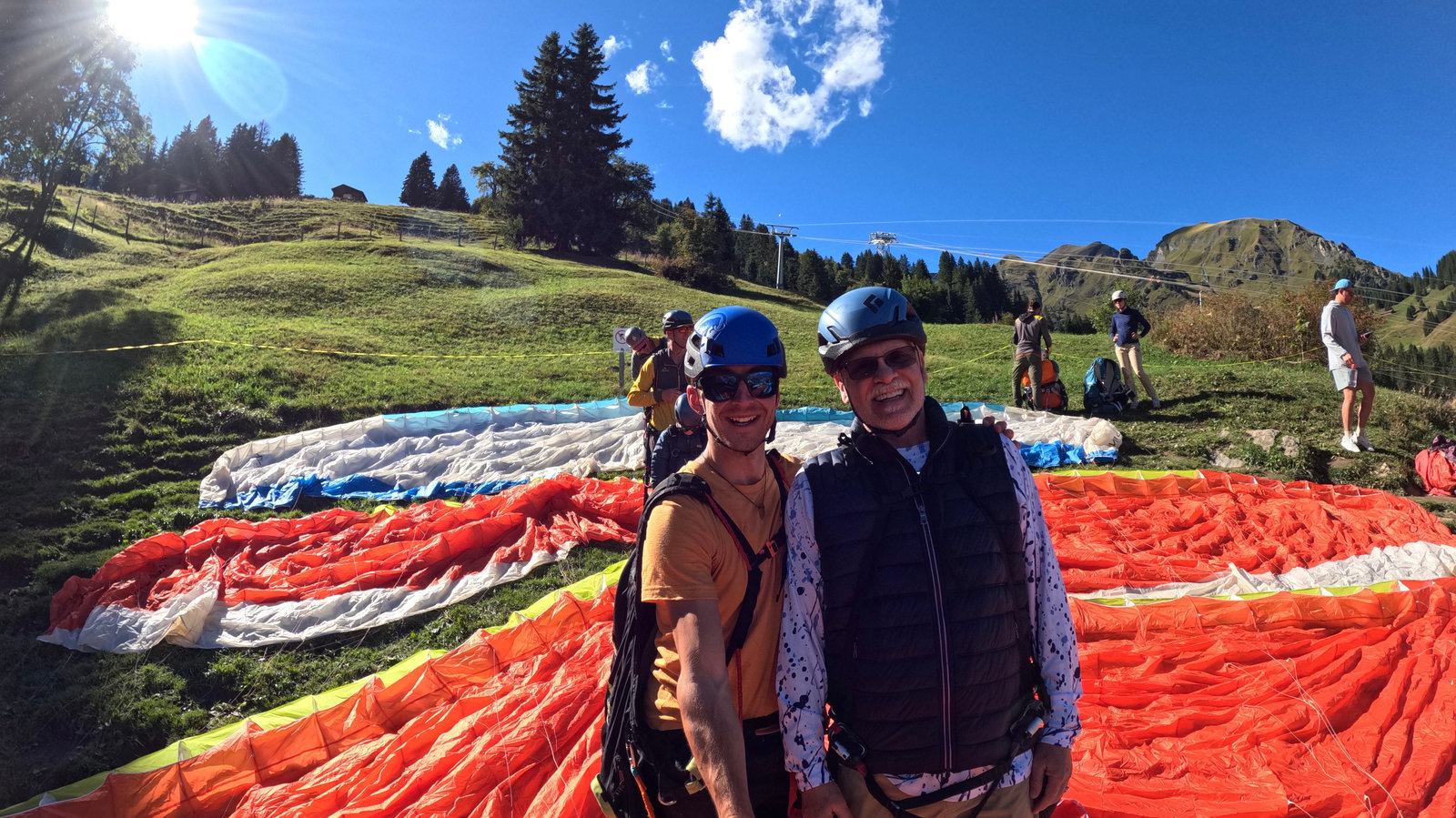 Dr. Peter Robbins and a companion beside a paraglider at a mountain launch site.